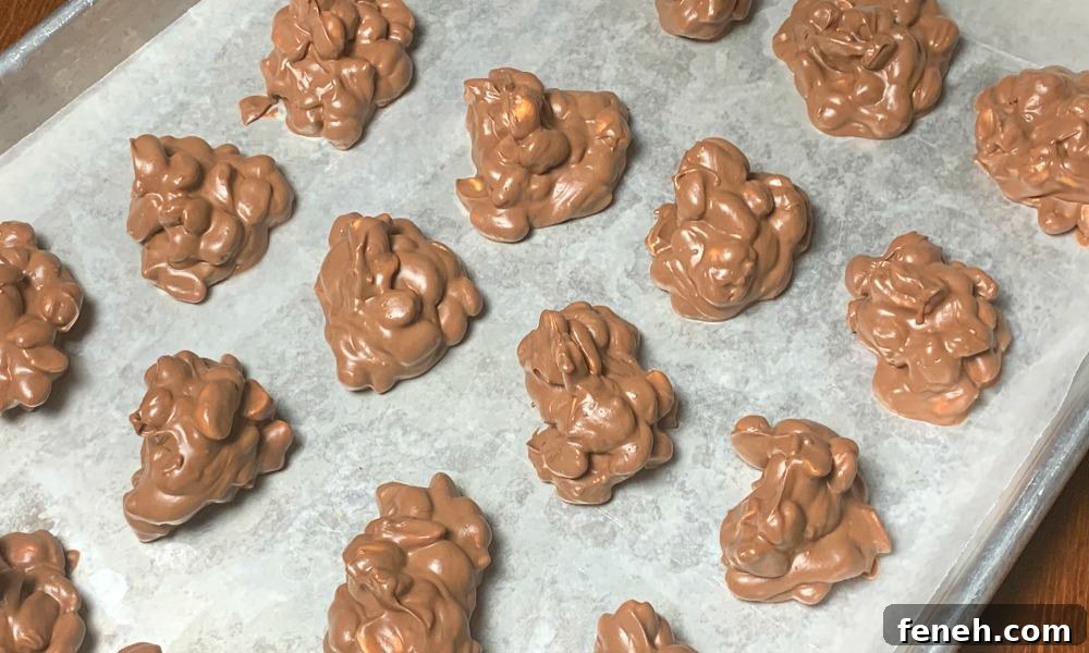 Clusters of chocolate covered peanuts on a wax paper covered baking sheet made from white almond bark, German chocolate, semi-sweet chocolate chips and dry roasted peanuts