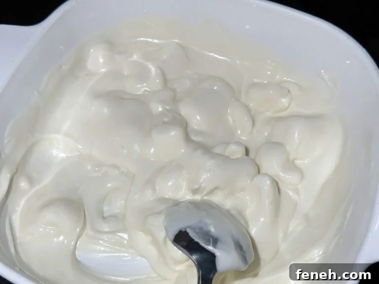 White almond bark melting in a white dish and being stirred with a spoon.