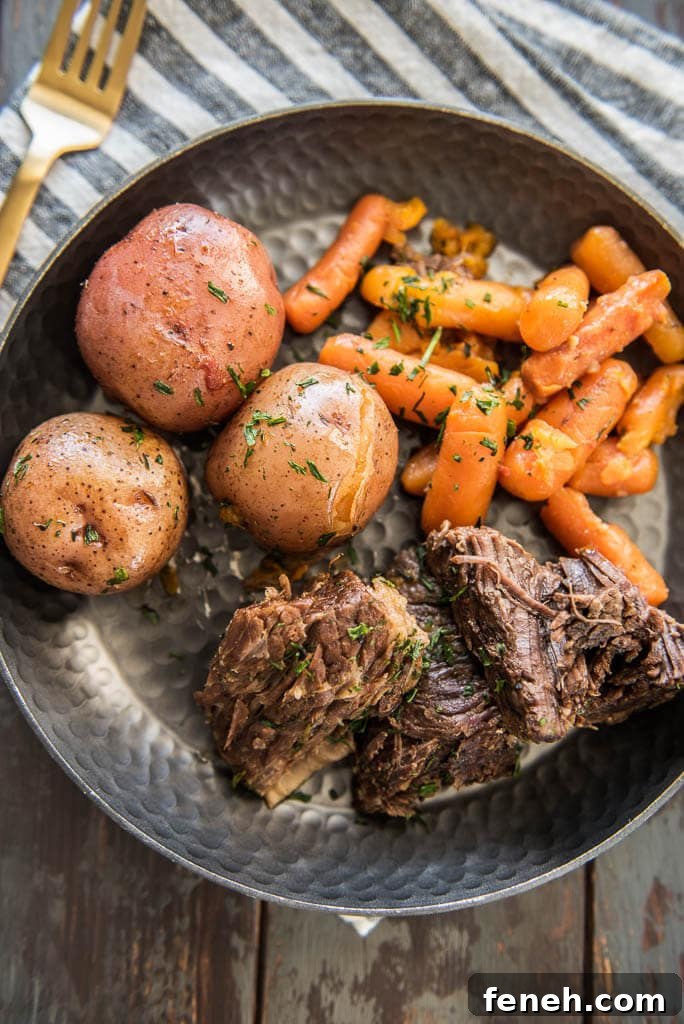 Pressure Cooker Pot Roast on a metal plate served with carrots and potatoes on a table with a gray and white napkin and gold fork