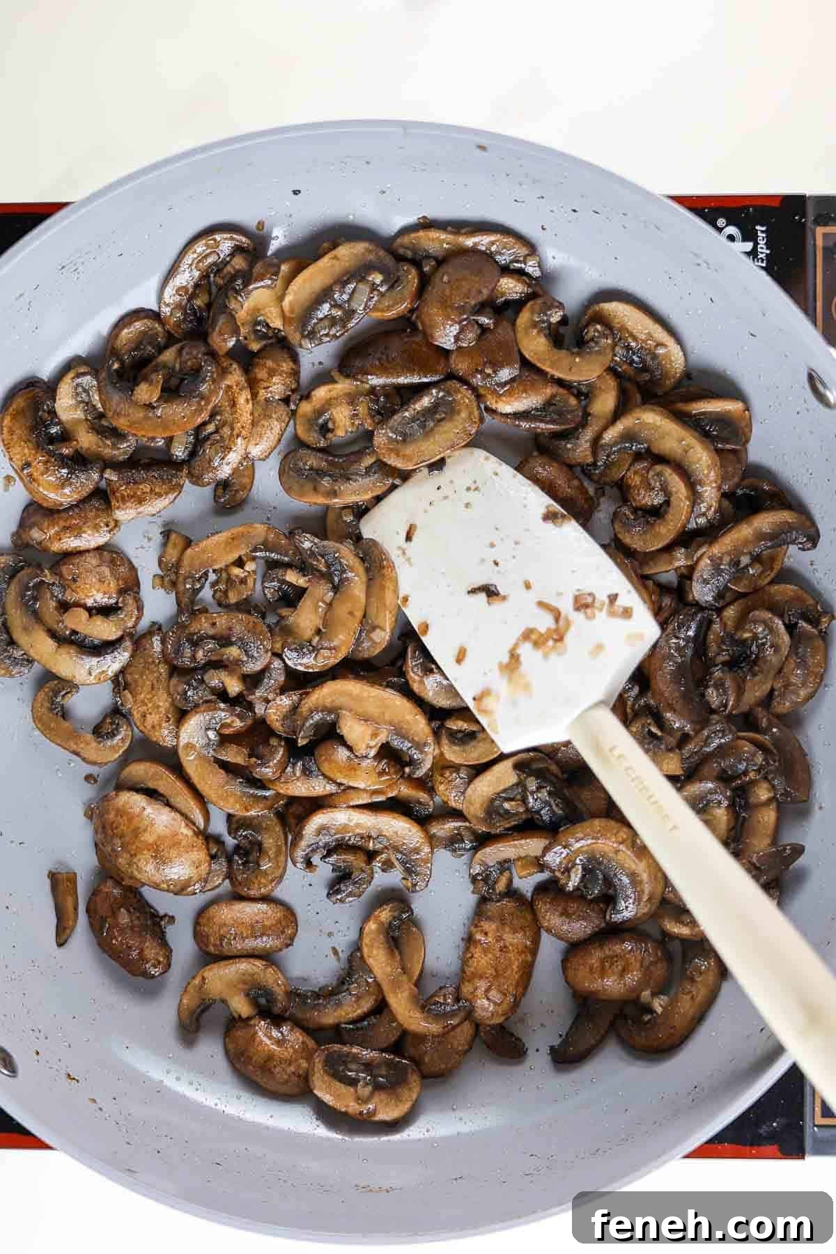 Sauteed mushrooms in a skillet with a rubber spatula.