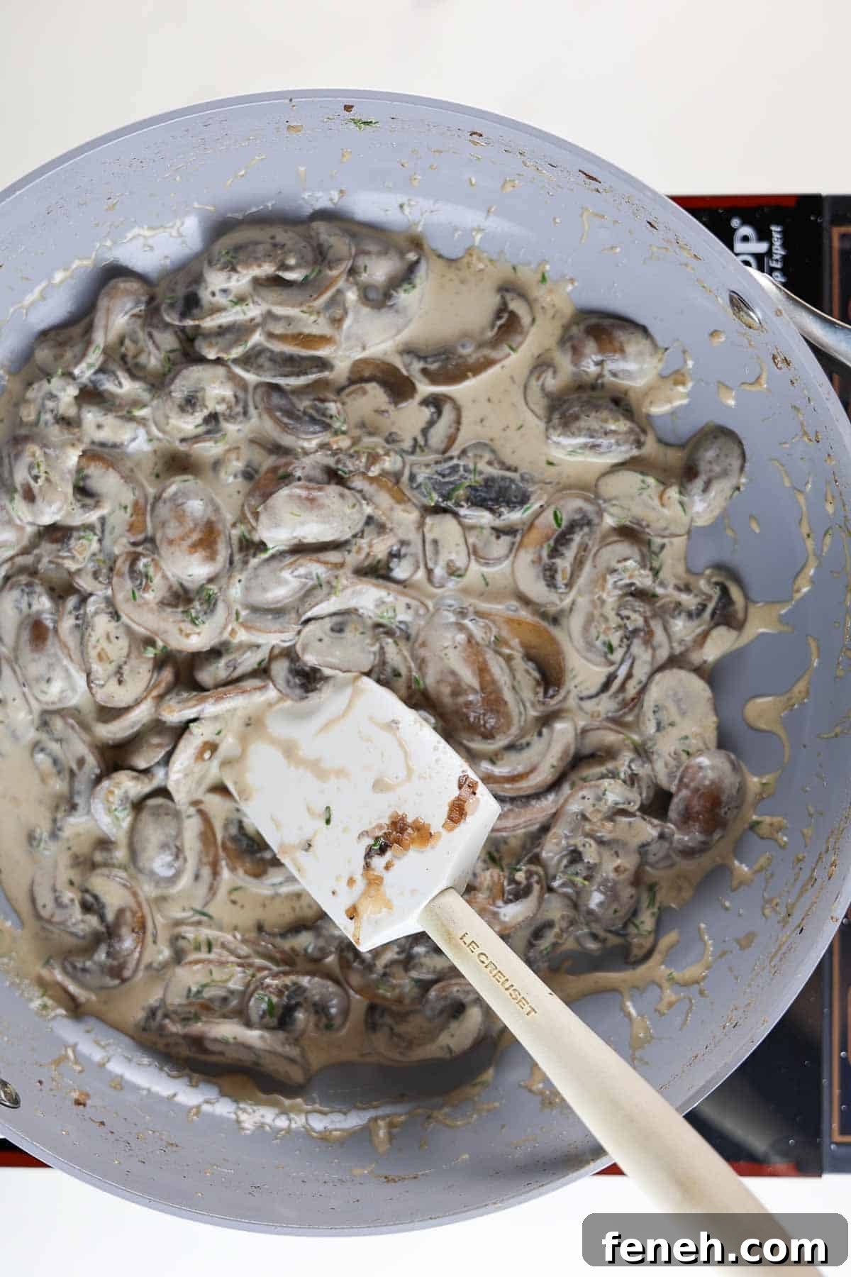 Mushrooms and cream in a skillet with a rubber spatula.