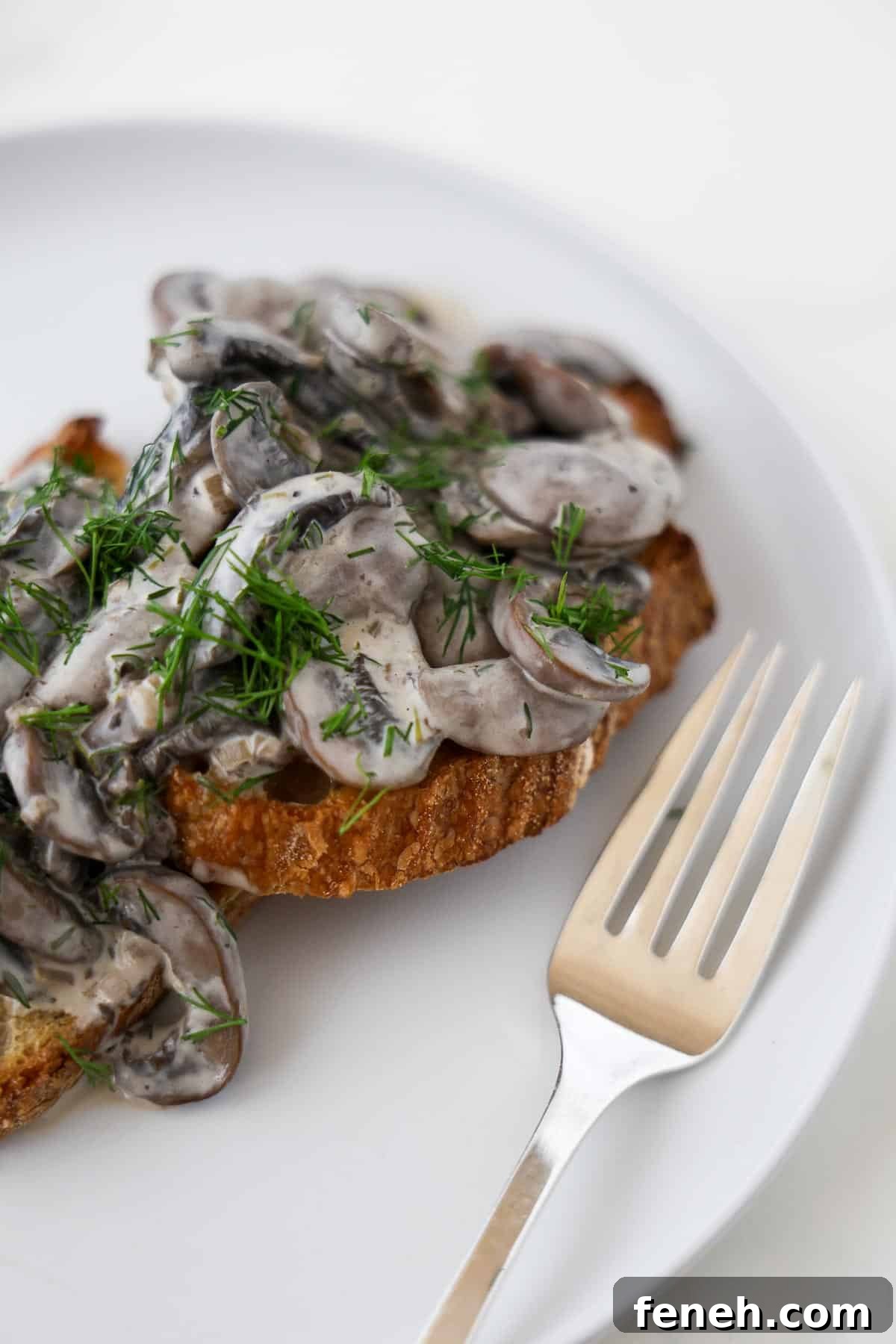 Creamy mushrooms on toast topped with chopped dill next to a fork.