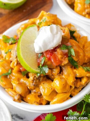 Small white bowl filled with taco mac and cheese, garnished with sour cream, salsa, chopped cilantro, and a lime slice.