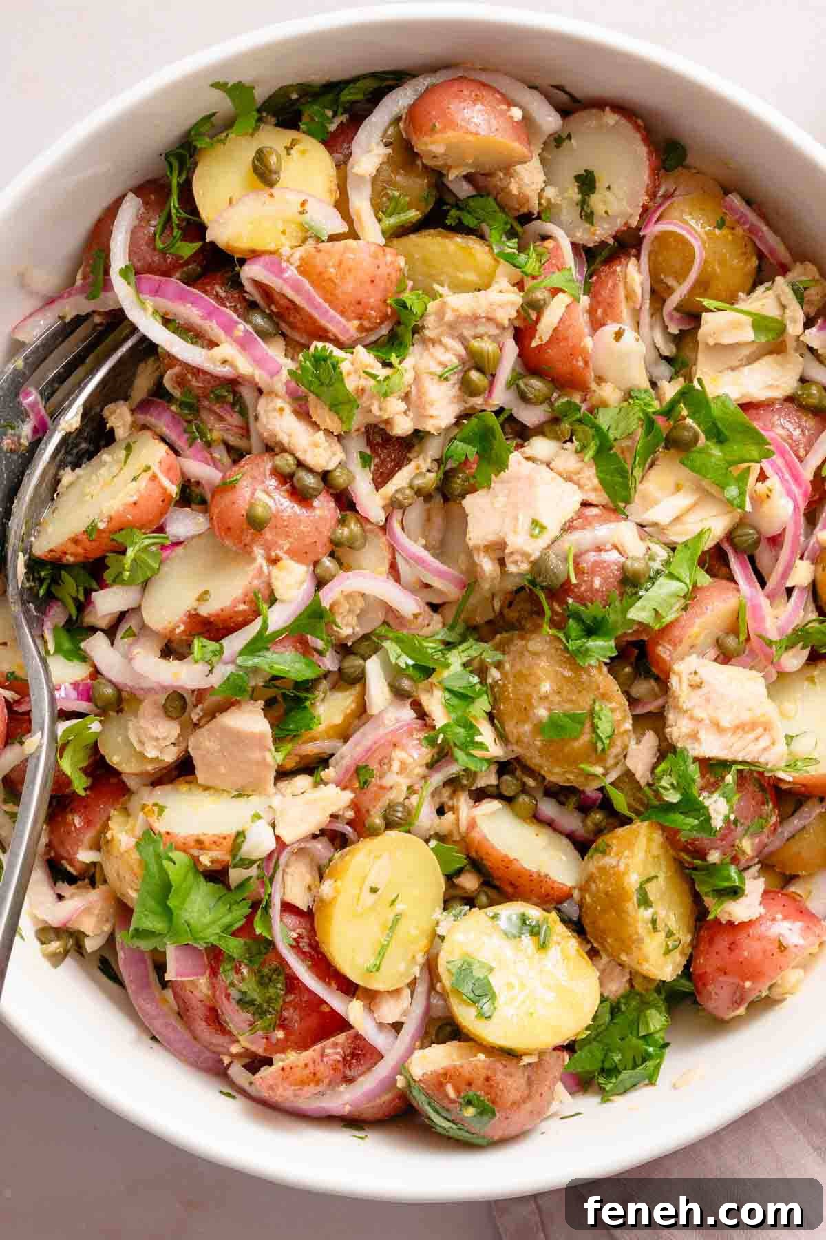 potato salad with tuna and red onions in white bowl.