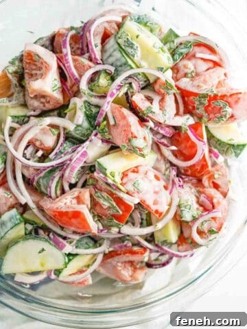 creamy cucumber tomato and onion salad in large glass bowl.