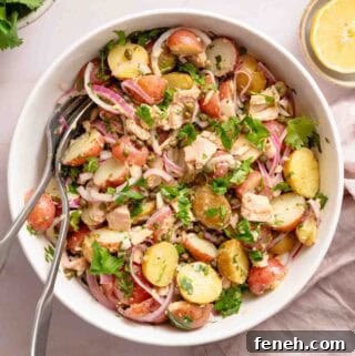 potato and tuna salad in white bowl with serving spoons.
