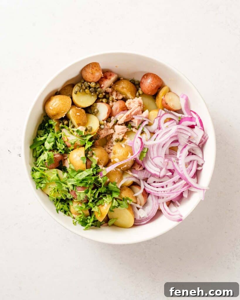 potatoes herbs tuna and sliced onion in white bowl.