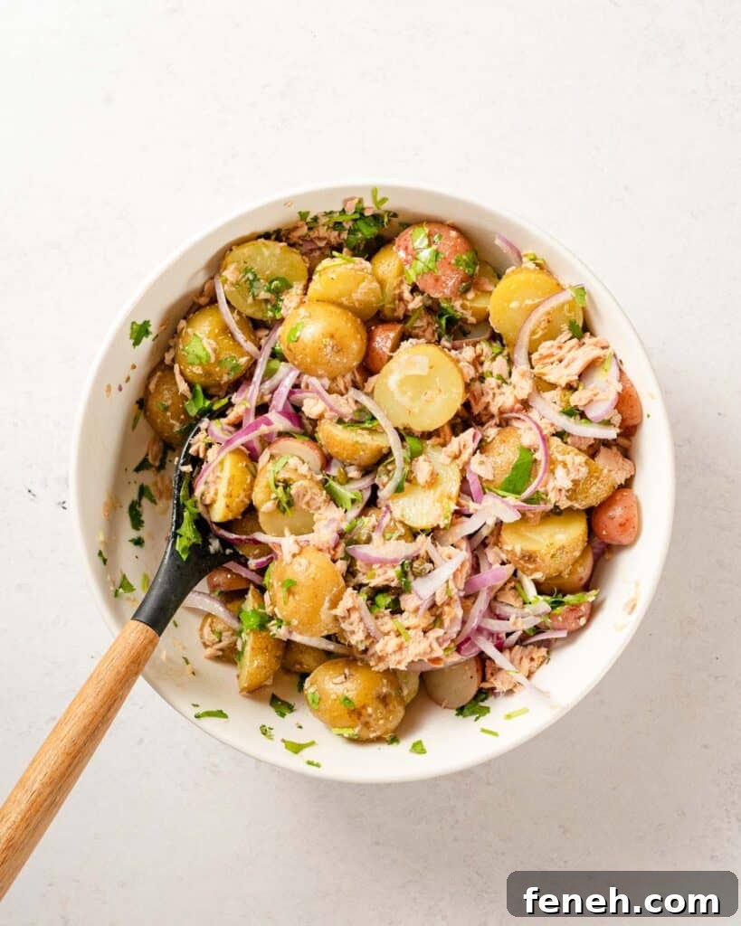 tuna and potato salad mixed in white bowl with wooden spoon.