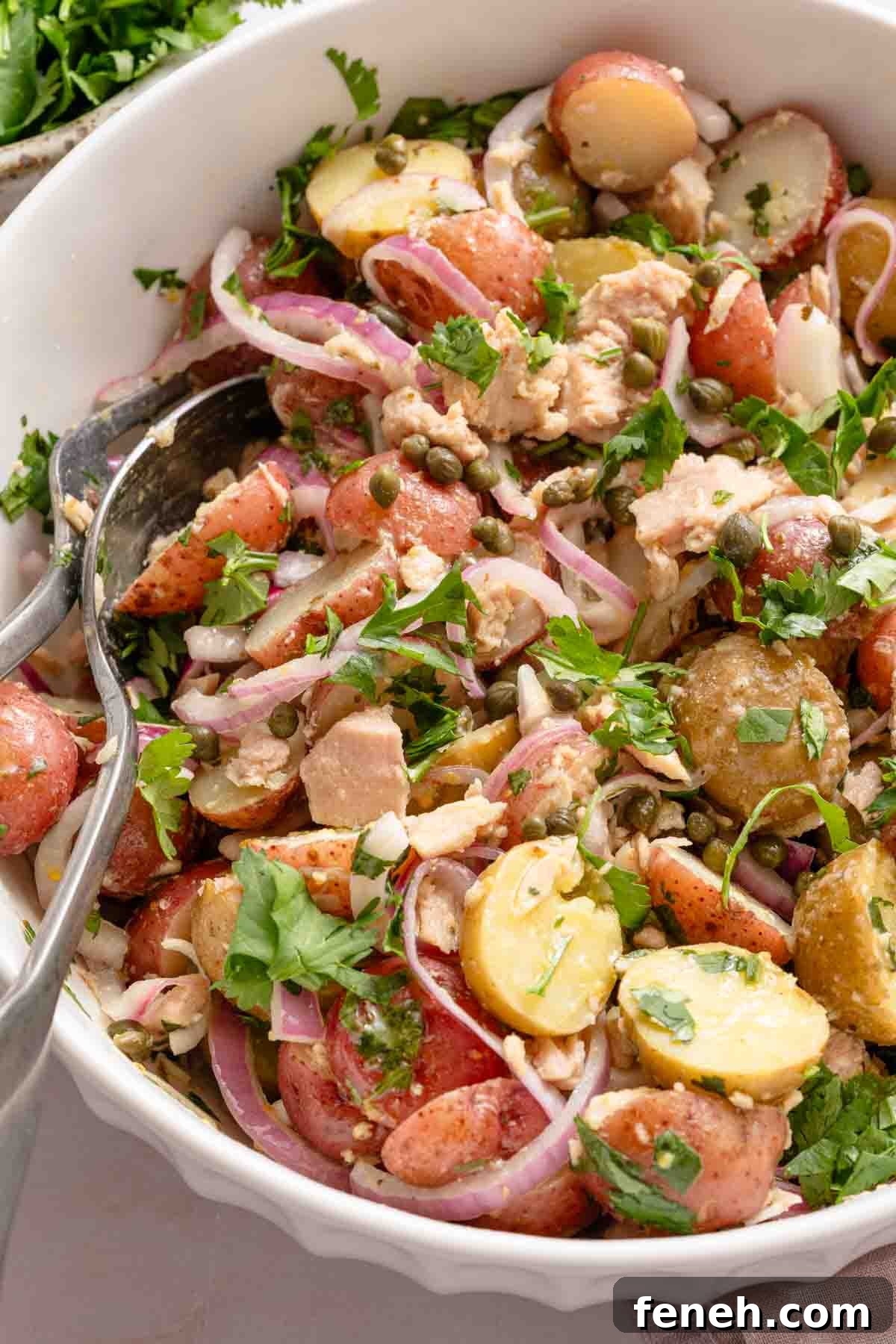 spoon scooping up tuna and potato salad from white bowl.