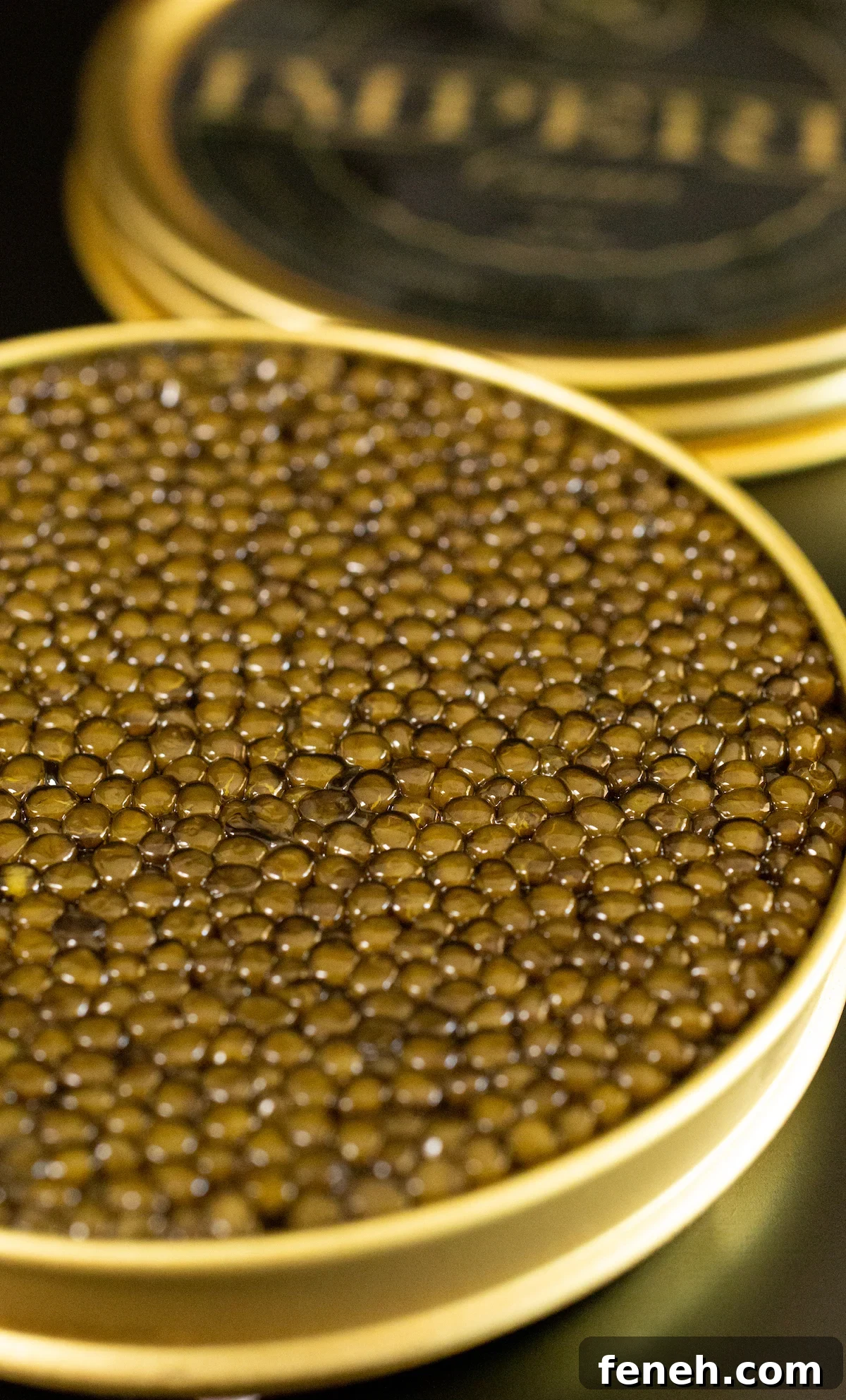 An open tin of golden osetra caviar sits on a black table