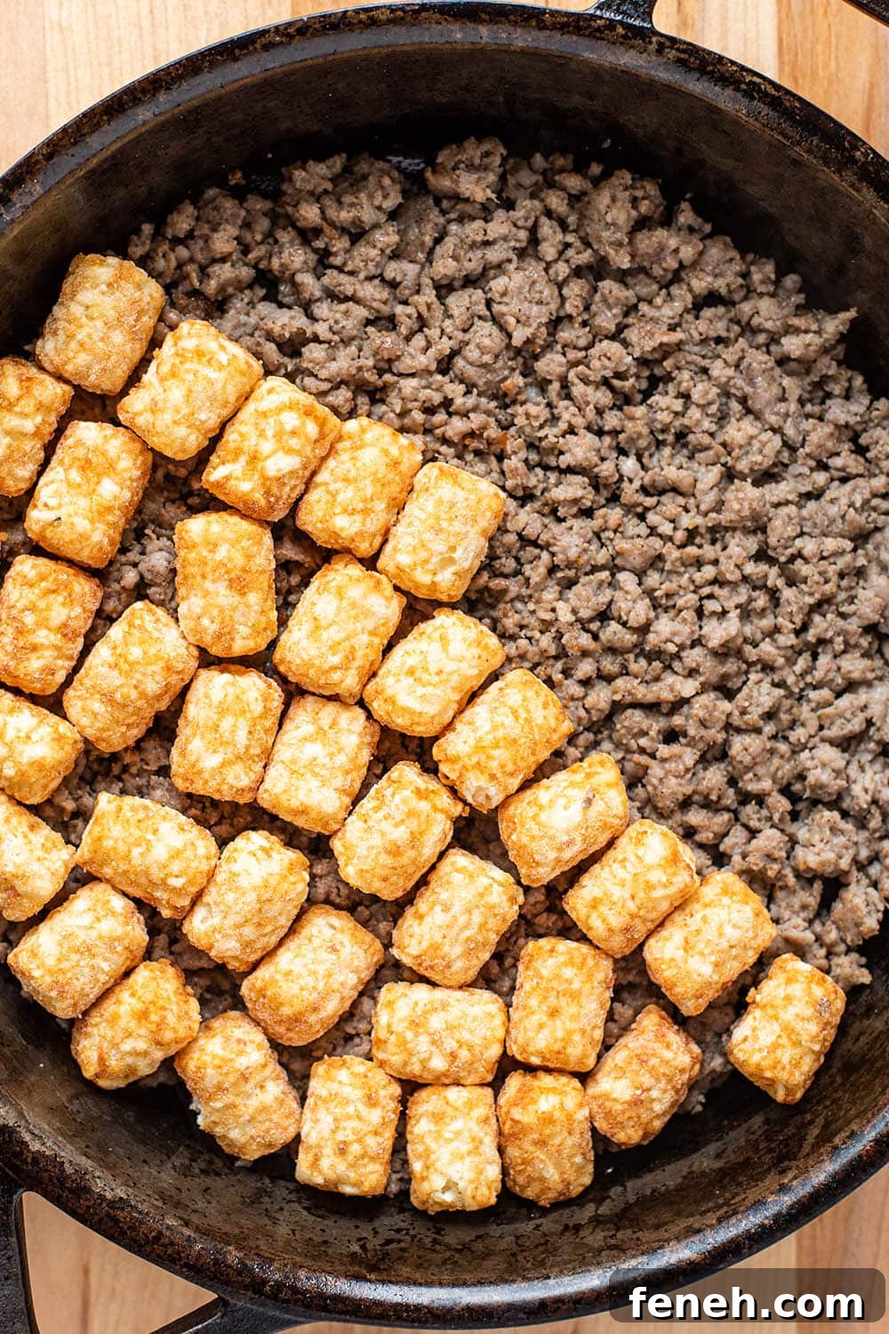 Cooked ground sausage being layered with frozen tater tots.