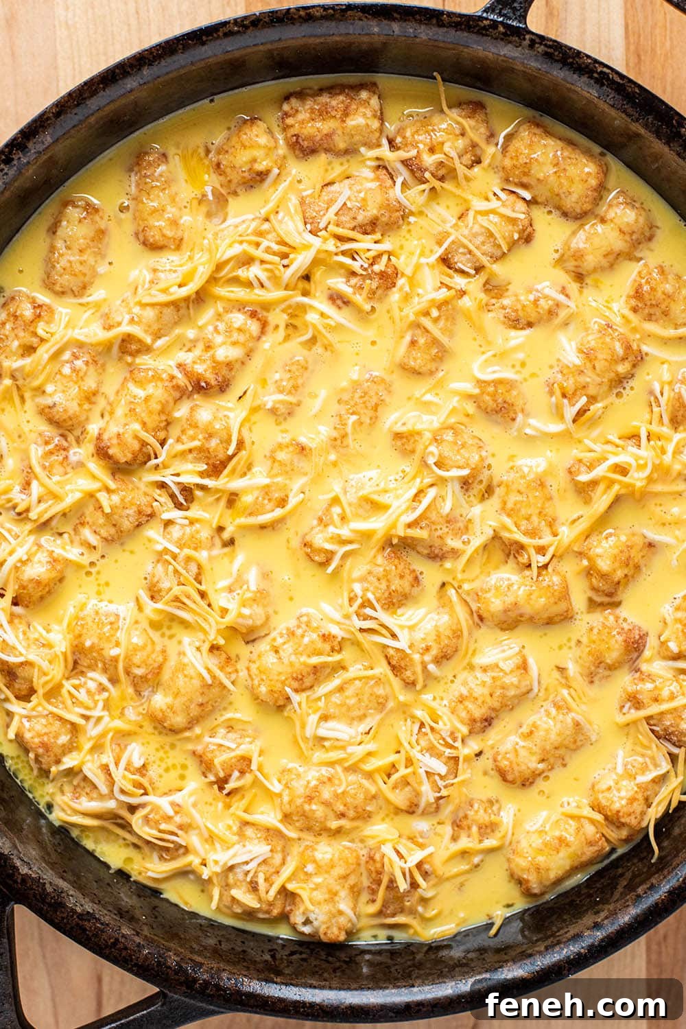 Whisked egg and shredded cheese pored over tater tots in a cast iron skillet.