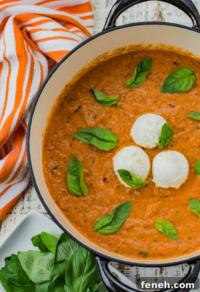 A pan of vodka pasta sauce with three dollops of ricotta cheese in the center. Basil leaves are scattered on top. A orange and white strip and a plate of basil leaves sit next to the pan.