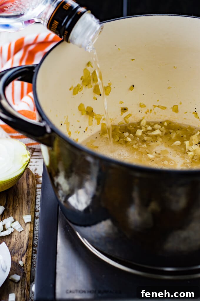 A black Dutch Oven with sauteed onions and garlic with vodka being poured into the pan.