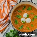A pan of vodka pasta sauce with three dollops of ricotta cheese and basil leaves sprinkled on the sauce. An orange and white striped napkin and basil leaves sit next to the pan.