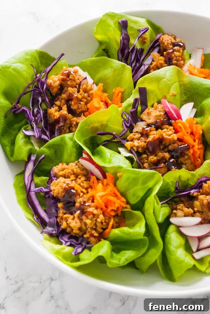 A plate containing vegetarian tempeh lettuce wraps with shredded carrot and red cabbage toppings.