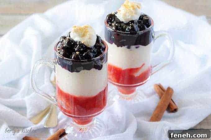 The finished blueberry cheesecake parfaits in mugs layered with strawberries, cheesecake, and blueberry toppings.