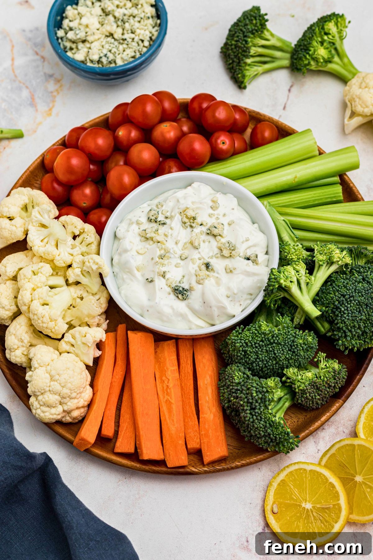 Creamy dip in a small round white bowl, topped with crumbled cheese, surrounded by freshly chopped veggies. 