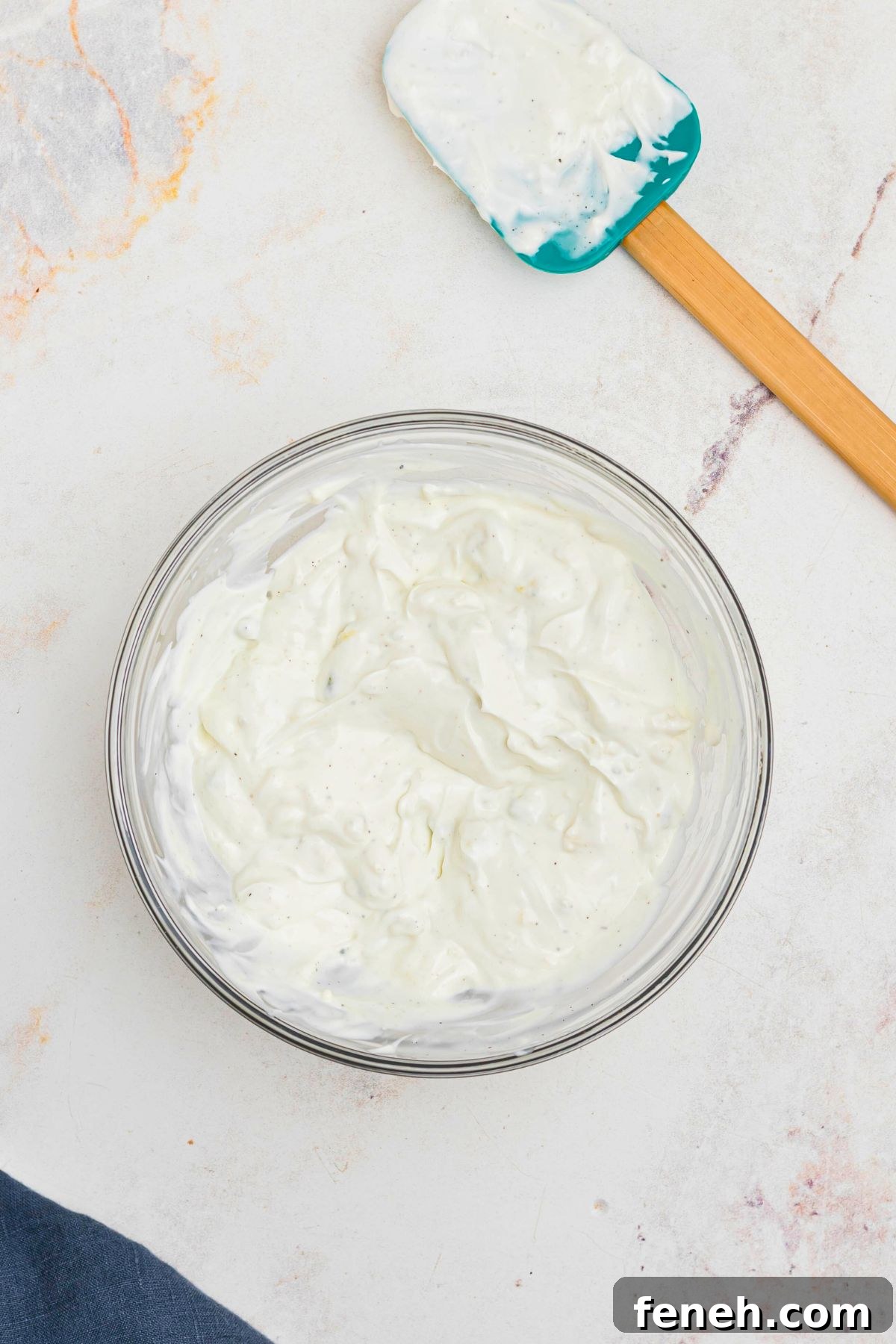 Clear glass bowl with dip  after being mixed together, with spatula on the table. 