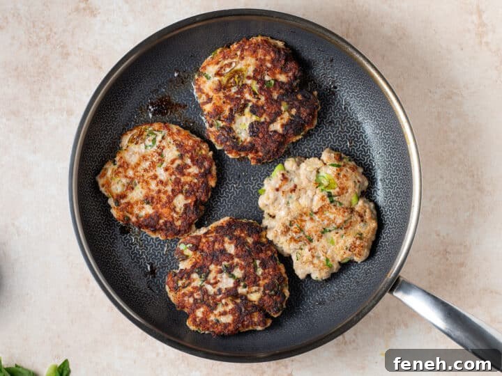chicken patties cooking in a skillet with a golden brown crust