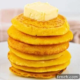 A stack of golden fried cornbread, topped with butter on a pristine white plate.