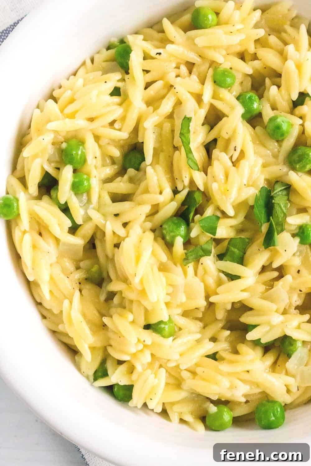 close-up overhead view of a white bowl filled with pressure cooker orzo made with lemon, parmesan, frozen peas, and fresh basil and parsley.