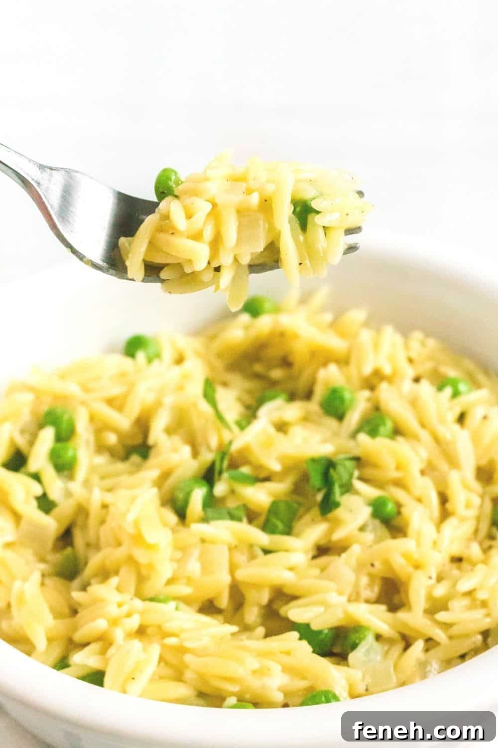 a fork lifts a bite of lemon parmesan orzo out of a white bowl