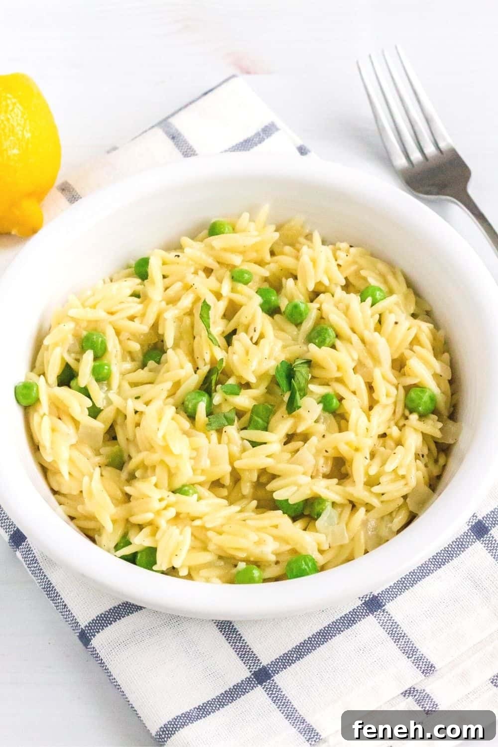 a white bowl of lemon parmesan orzo cooked in the instant pot is placed on a blue and white napkin. A lemon and fork are in the background.
