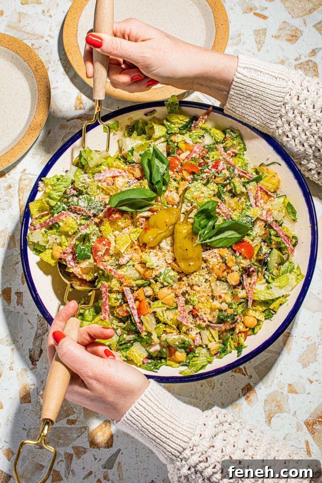 hand tossing chopped salad in large bowl with fork