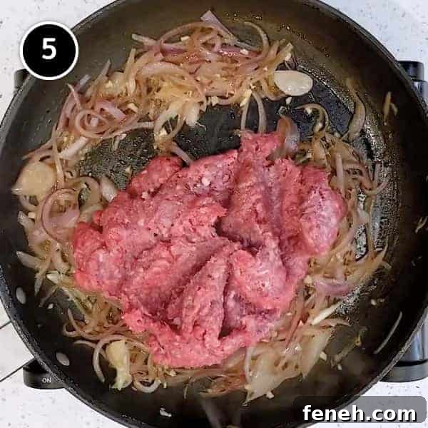 Adding ground lamb to fried onions in a small pan.