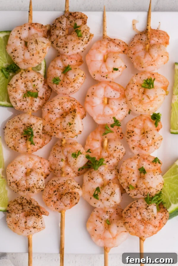 Overhead of shrimp skewers on a white plate with sliced limes.
