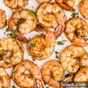 Juicy seasoned shrimp on a white plate garnished with parsley flakes