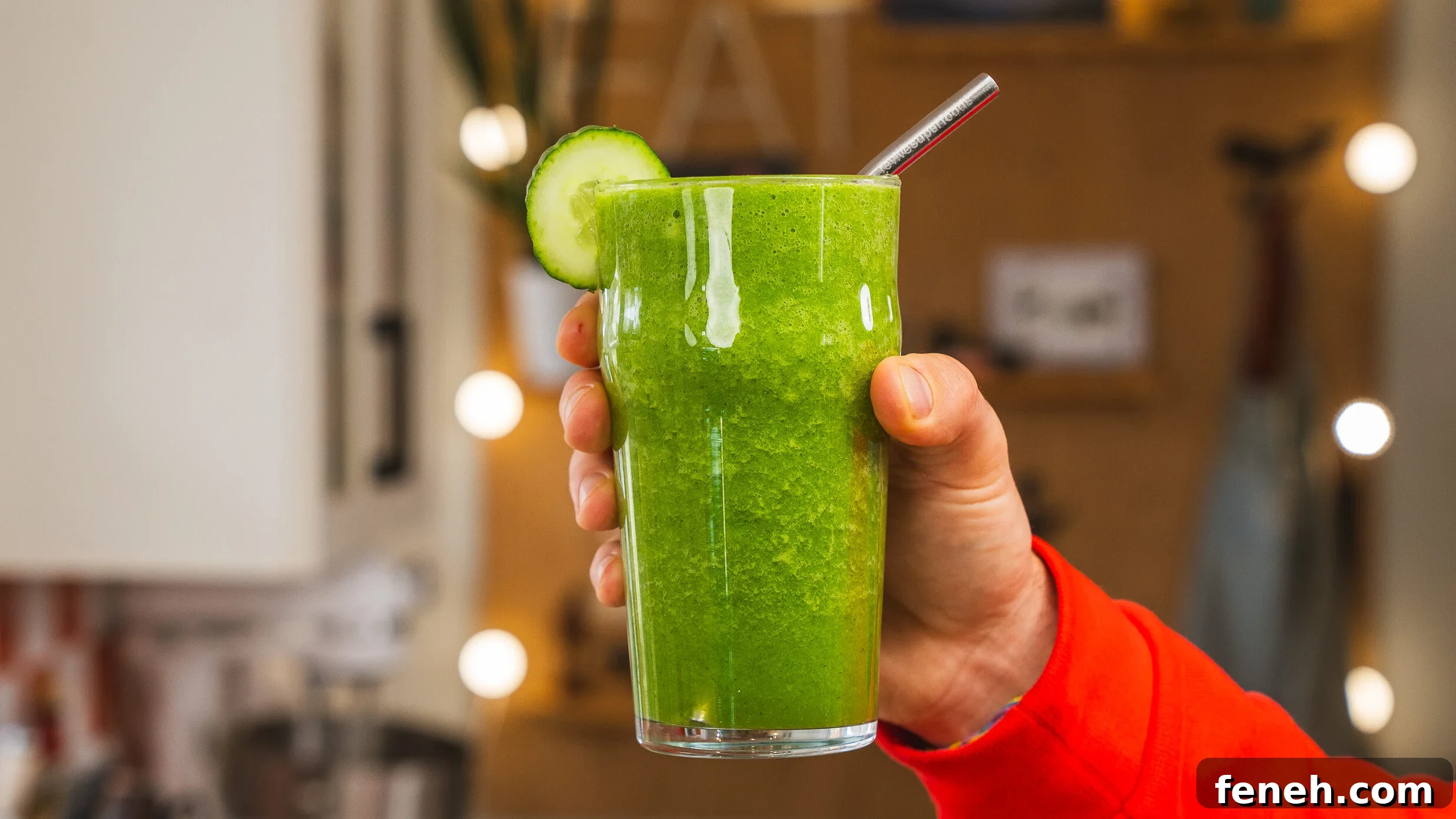 Someone holding a glass of green juice with a lime slice on the edge of the glass and a straw inside.