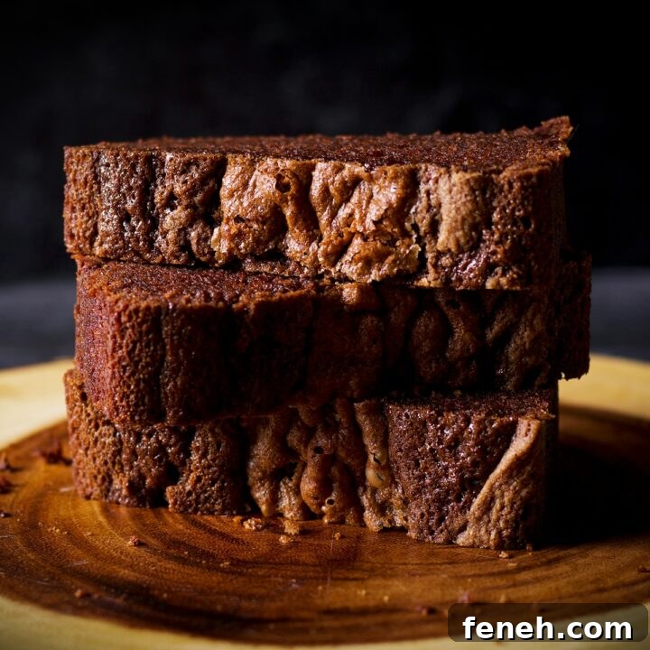 Three pieces of chocolate loaf cake stacked on top of each other on a wood serving board.