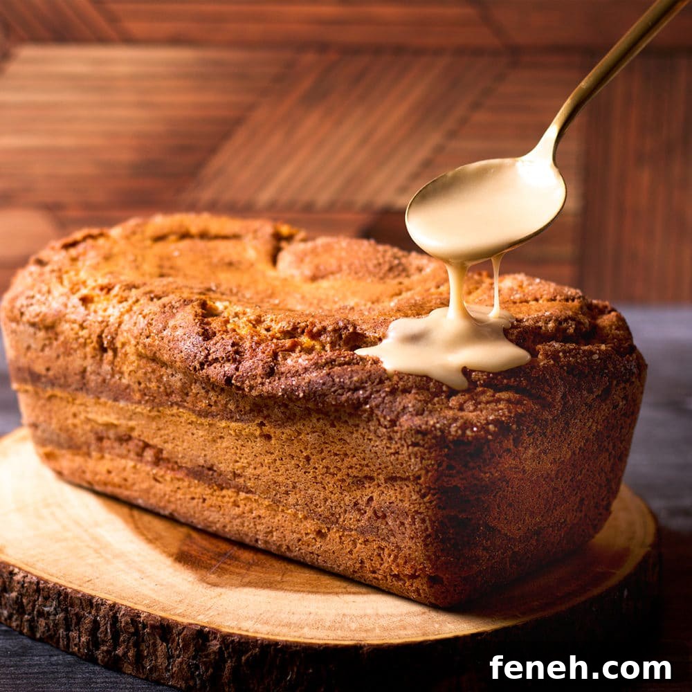 Someone using a gold spoon to drizzle vanilla icing over the top of a cinnamon loaf cake.