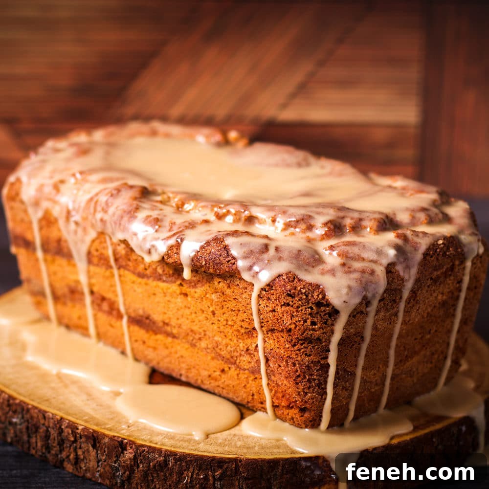 A cinnamon loaf cake covered in vanilla icing sitting on a wood cutting board.