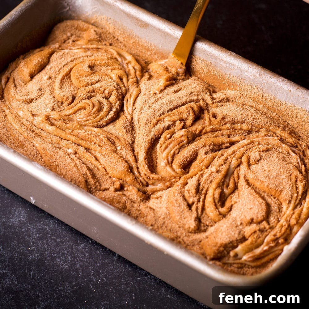 Someone using a knife to swirl layers of cake batter and cinnamon sugar in a loaf pan.