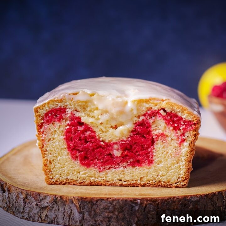 A raspberry swirl loaf cake on a wood cutting board that's been cut in half so you can see the bright red ribbon of raspberry cake swirled into the loaf.