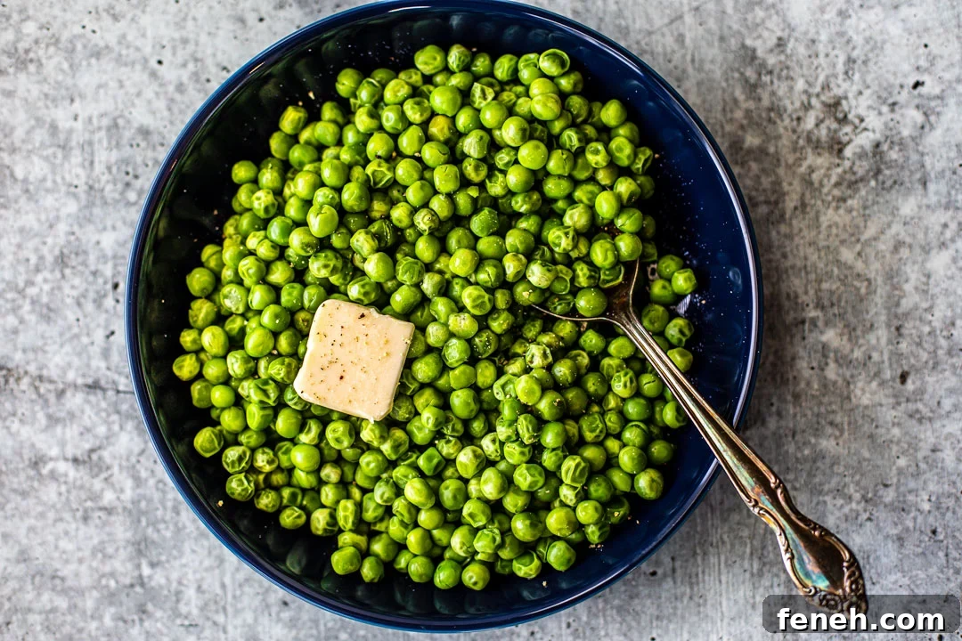 Bowl full of bright green peas with a pat of melting butter on top.
