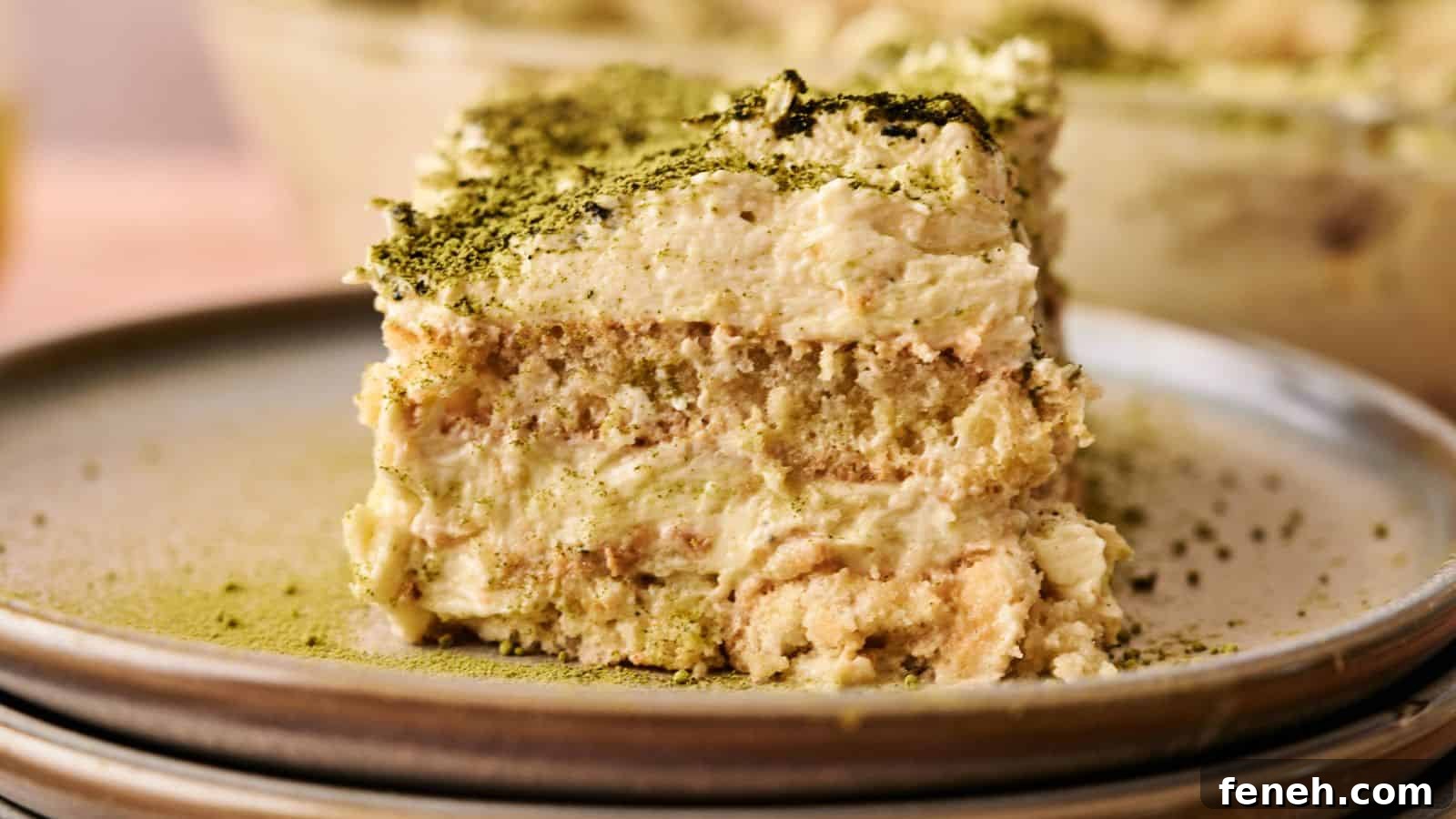 A close-up of a slice of tiramisu topped with green matcha powder, served on a ceramic plate.