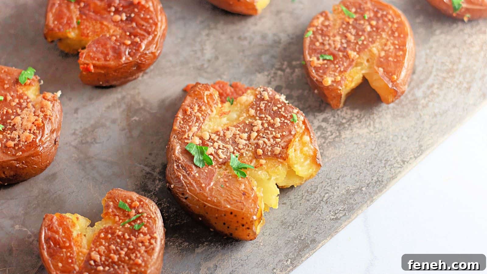 Several smashed, roasted baby potatoes garnished with herbs and grated cheese are arranged on a baking sheet.