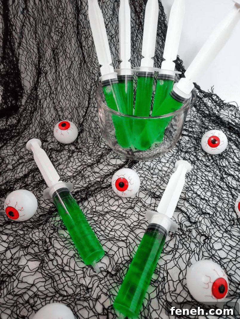 Halloween Shot Recipes and Spooky Shooter Ideas for Parties 6 Green jello in syringes with halloween decorations.