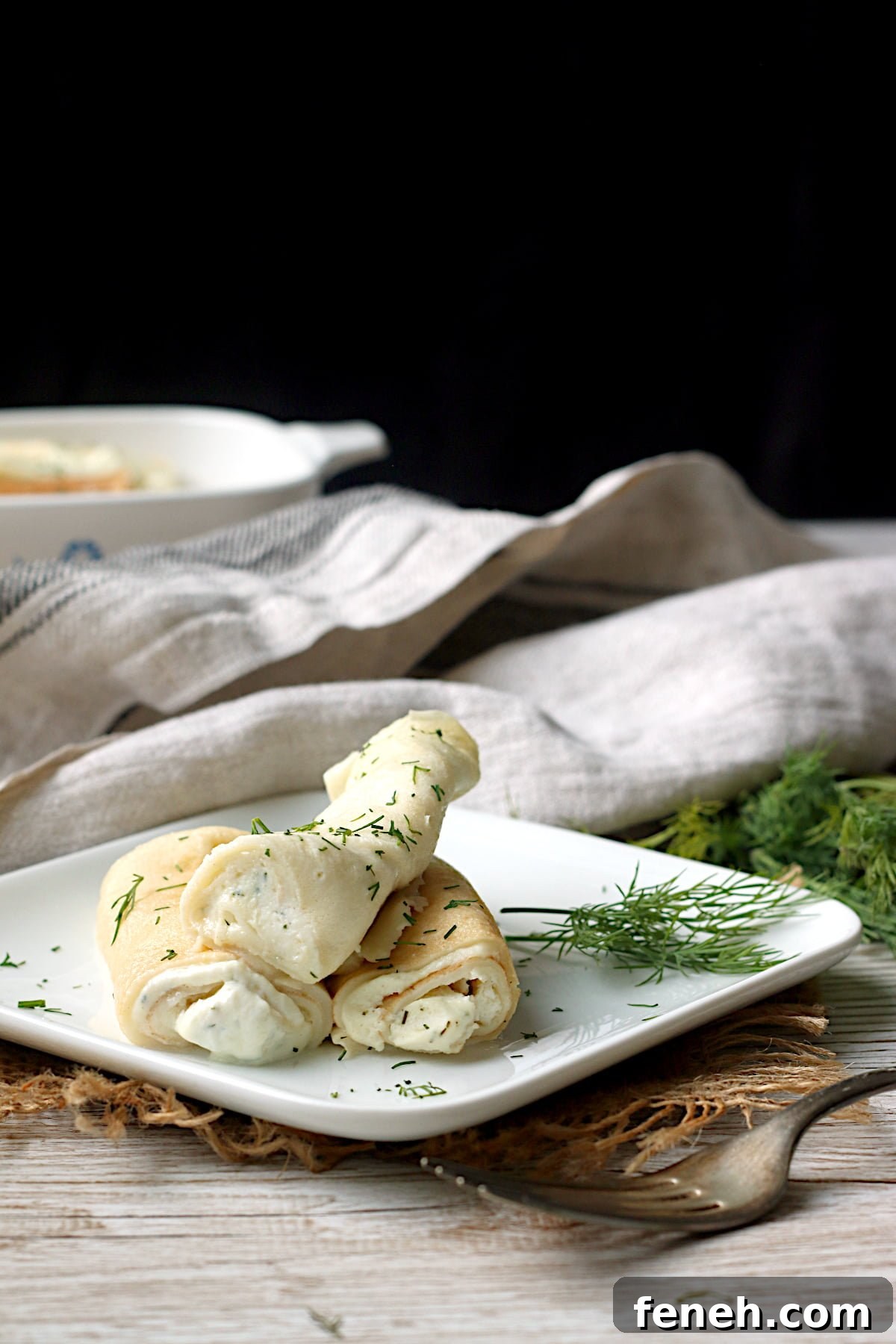 Nalysnyky (Savory Ukrainian Crepes with Dill and Cottage Cheese) on a small, square, white plate.