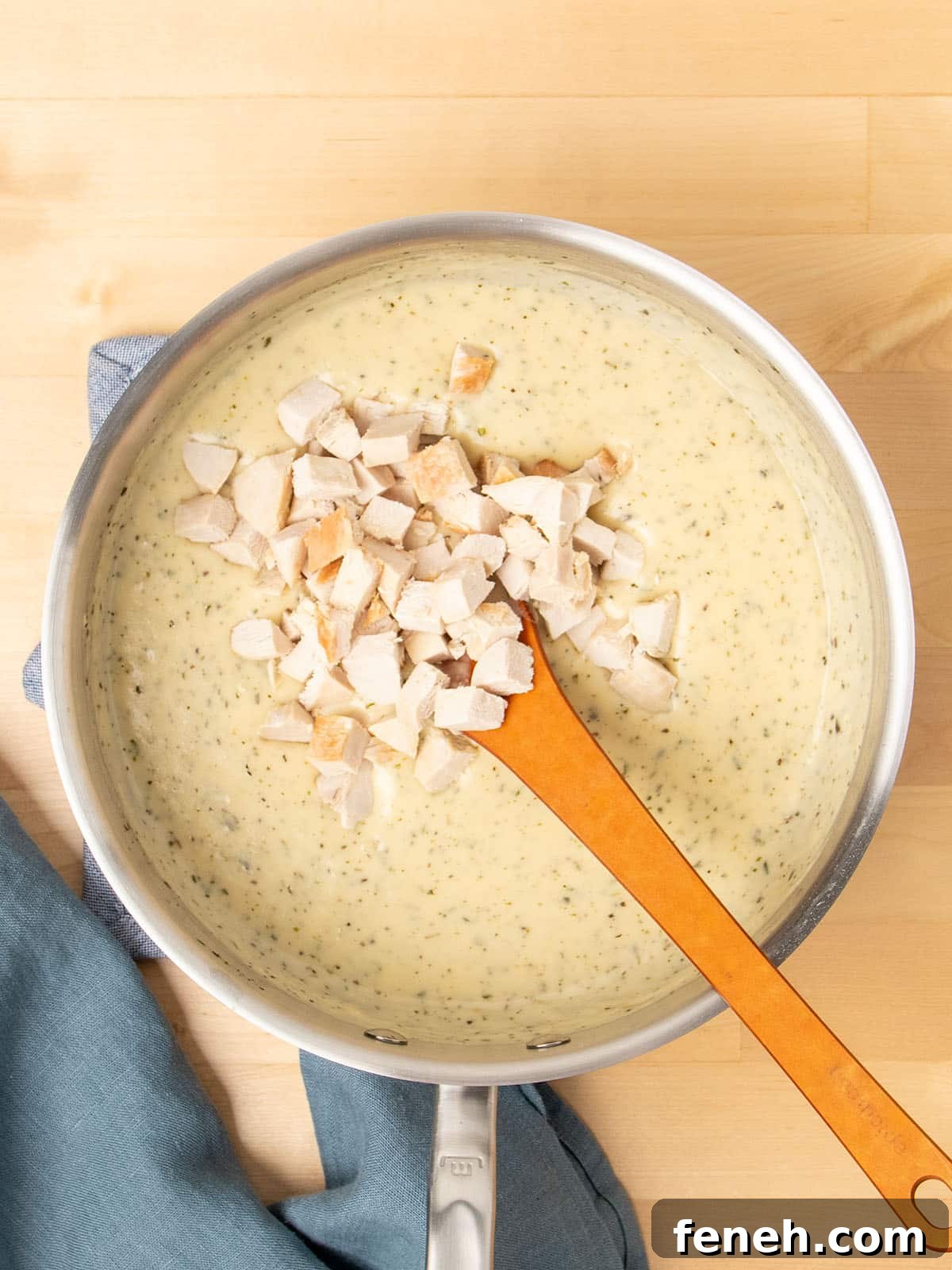 metal saucepan with cream of chicken soup with mixing spoon and chopped cooked chicken on top with blue cloth