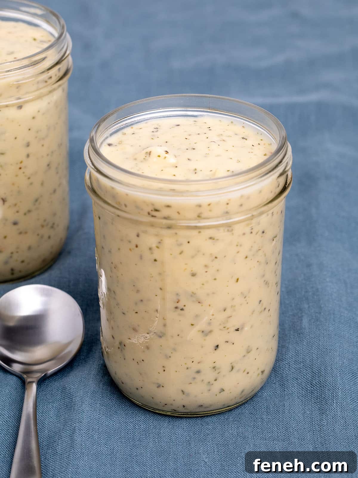 2 glass mason jars with light brown cream of chicken soup with herb flecks on blue cloth and one metal soup spoon on cloth