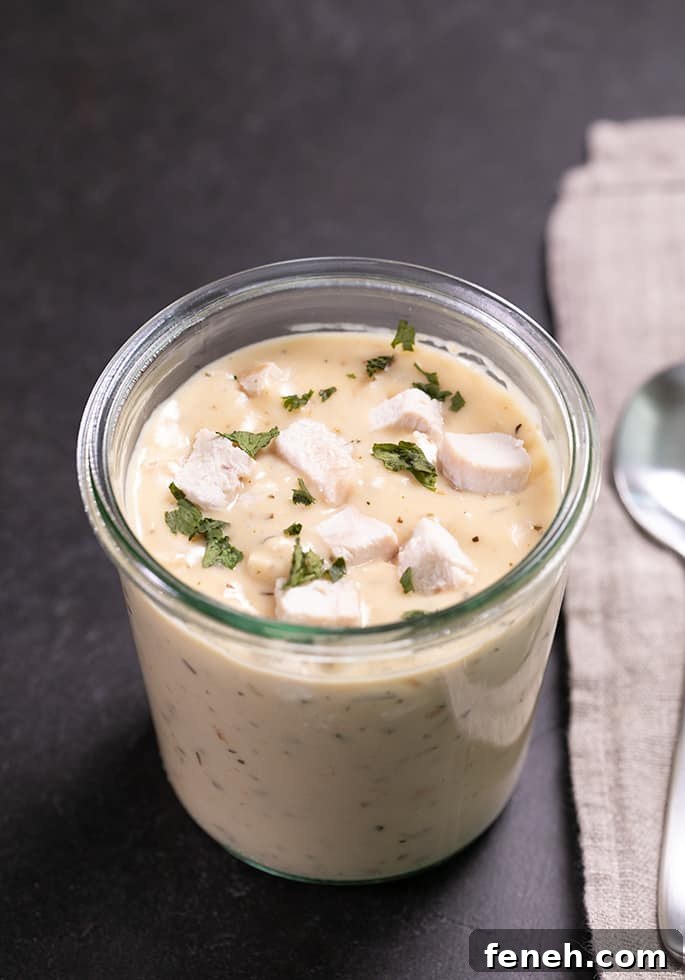Cream of chicken soup in a glass jar with parsley pieces on top and a clean spoon on a cloth