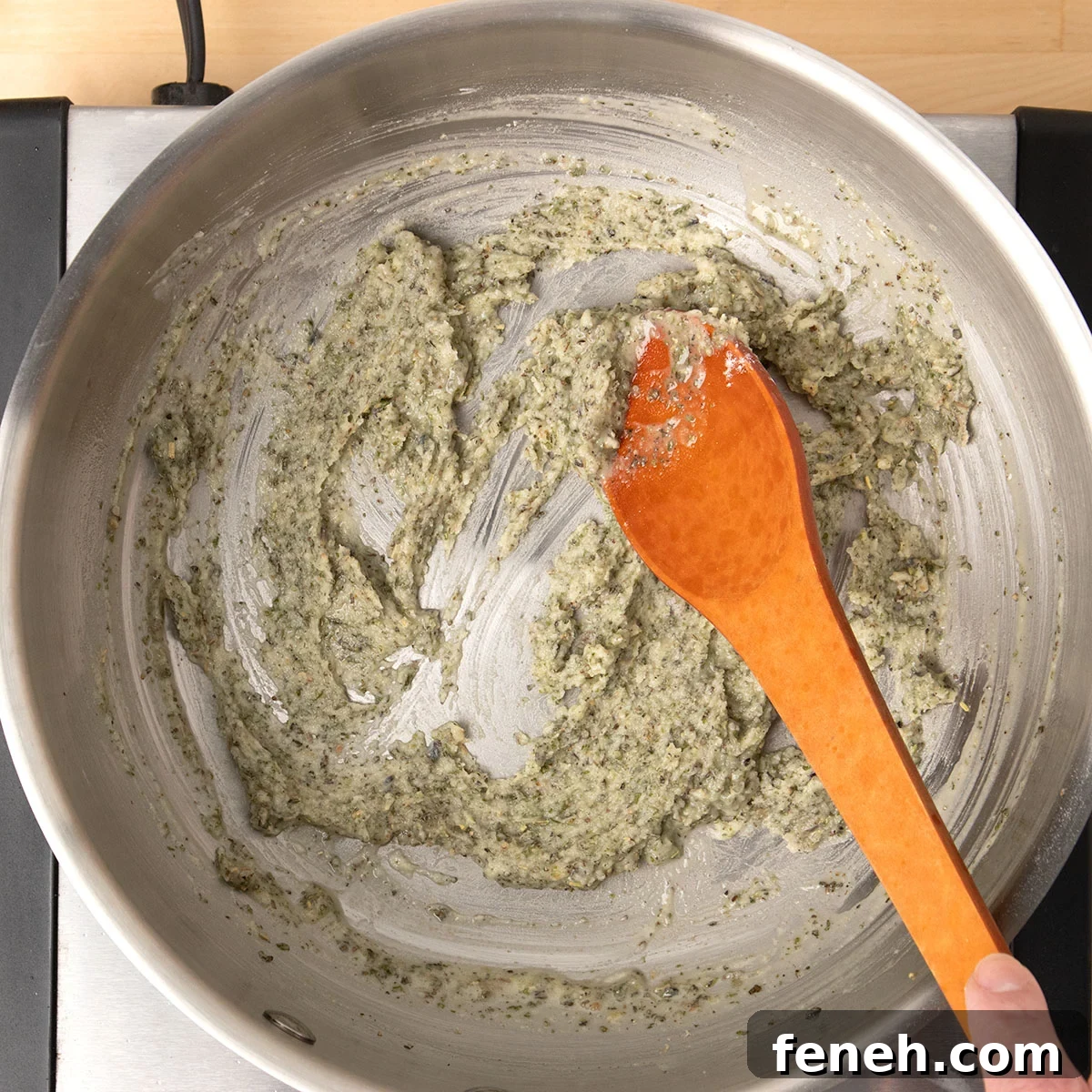 brown mixing spoon stirring light green flecked paste in same saucepan