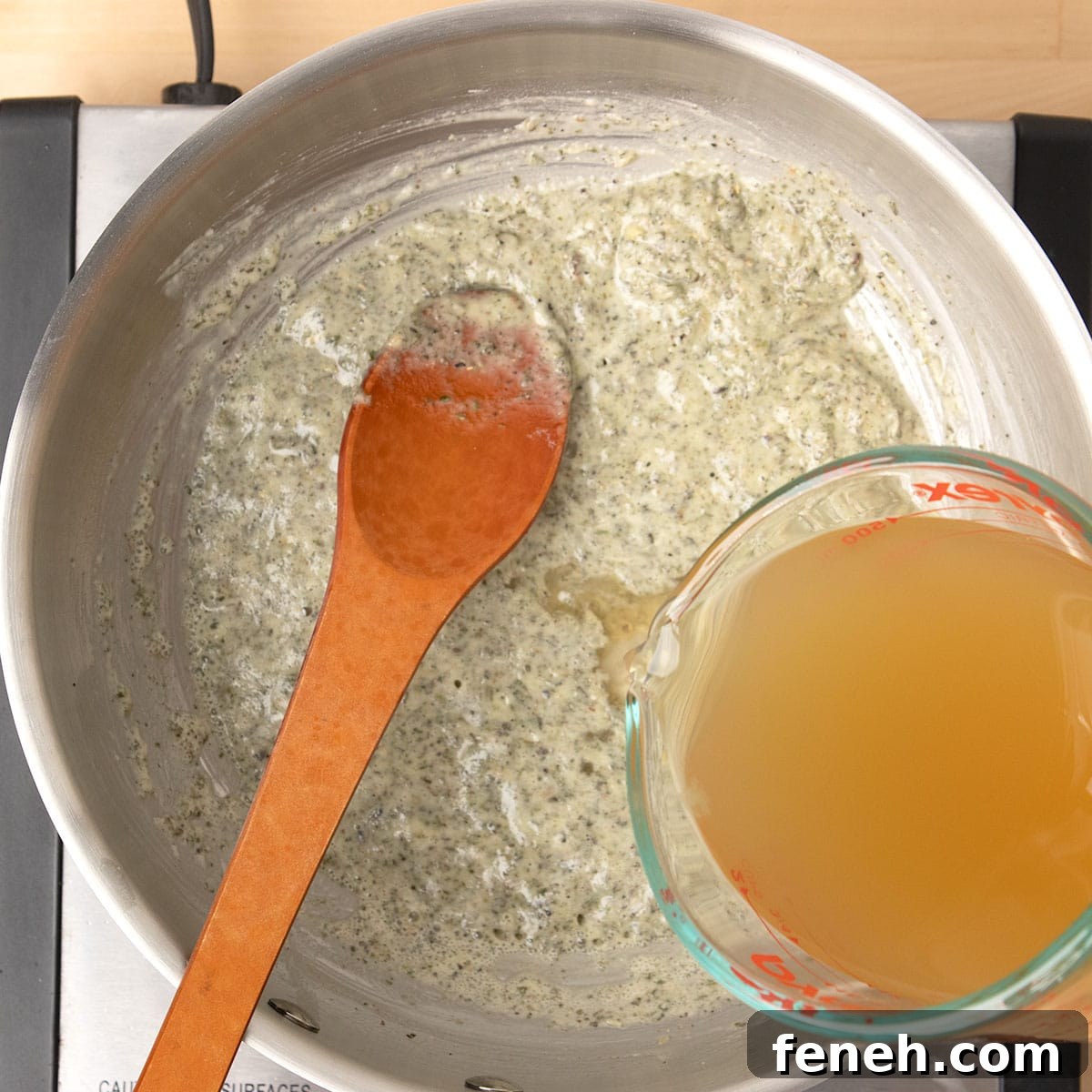 glass measuring cup pouring chicken stock into same saucepan