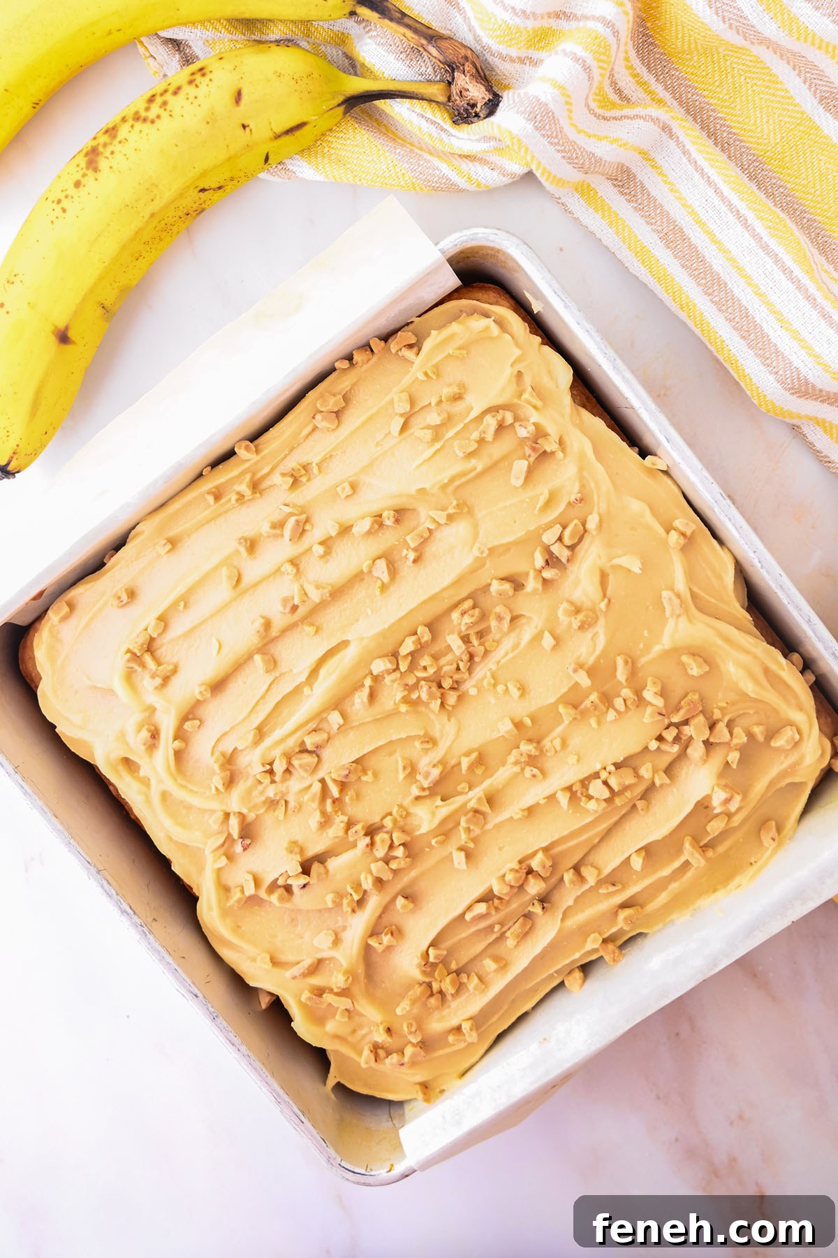 Banana Blondies with brown sugar frosting topped with nuts in parchment paper lined square baking pan.