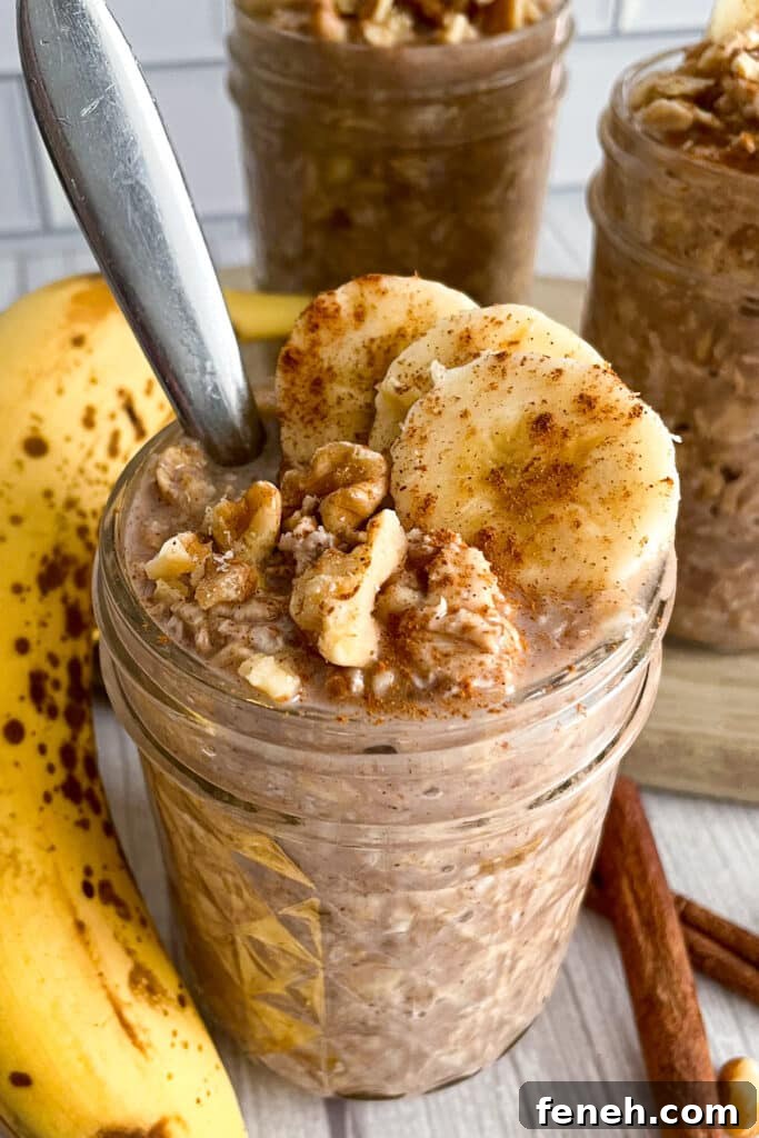 banana bread overnight oats in a mason jar with a spoon in it for serving.  Topped with sliced bananas and walnuts